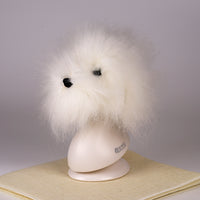 A white synthetic fiber dog wig displayed on a mannequin head, resembling a fluffy dog with black eyes and a pink collar.