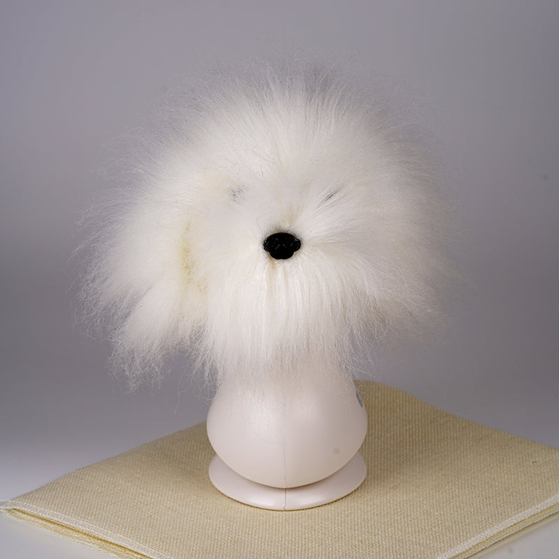 A white synthetic fiber dog wig displayed on a mannequin head, resembling a fluffy dog with black eyes and a pink collar.